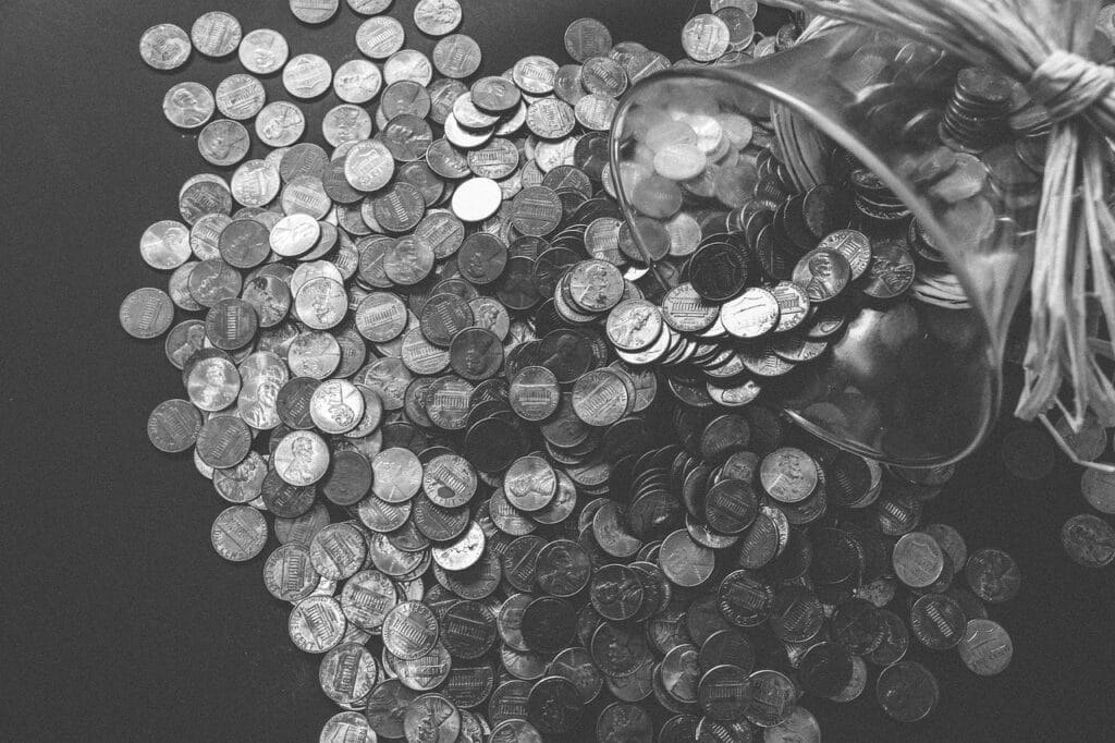 A glass jar tipped over with coins spilling out onto a dark surface, showing savings and loose change.